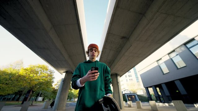 Handsome student looking mobile phone and walking at city closeup