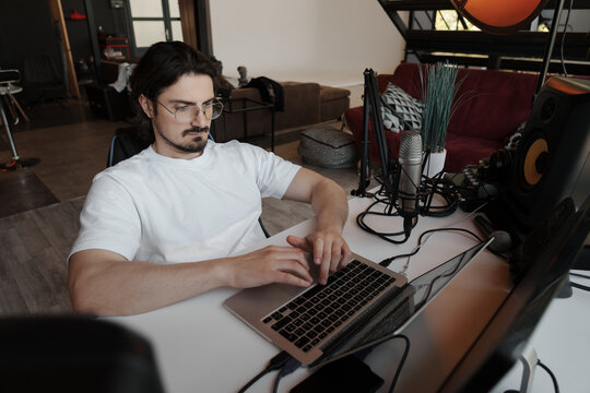 In his home studio, a music producer is engrossed in editing tracks on his laptop, surrounded by professional audio equipment