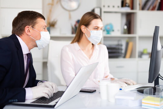 Focused Businessman In Disposable Face Mask And Rubber Gloves Working With Female Assistant In Office. Necessary Precautions During COVID 19 Pandemic..