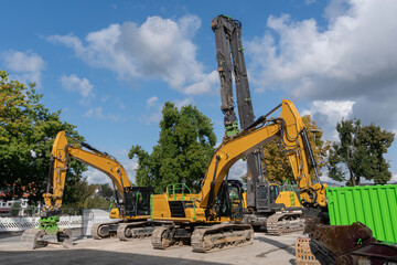 Large excavators standing on a construction site under a blue sky with light clouds.