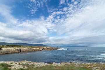 A scenic coastal landscape with rocky shores, blue ocean waves, and a sky filled with fluffy white clouds
