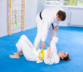 Coach teaches a young woman techniques for wrestling and throwing on sports mats during judo...