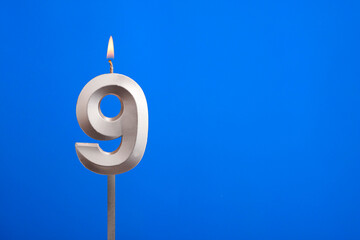 Birthday number 9 - Candle lit on blue background