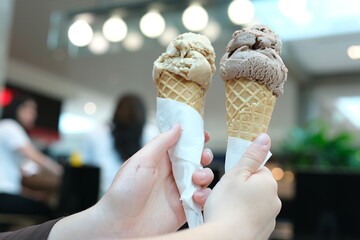 Two servings of ice cream cone on background of Mall, two girls clinking together with a brown, like glasses, game of communication, Friendship, eating delicious dessert. chocolate ice cream