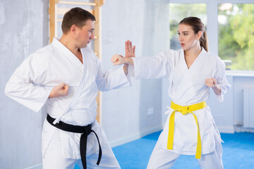 Active young girl and middle-aged man practicing kicks and blocks in pair during karate courses