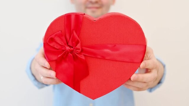 Young man in glasses hold heart gift box on white background. Valentines day,anniversary,birthday concept