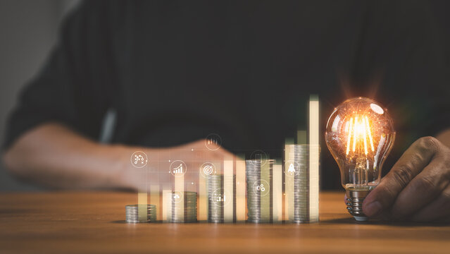Adult man hand holding a light bulb and money stack on table. New ideas for savings money, taxes, retirement, working, small business, finance, investment, financial planning, and financial concept.