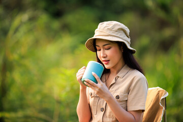 asian woman in safari dress sitting on chair drinking coffee cup in the nature,  adventure and campground travel concept,