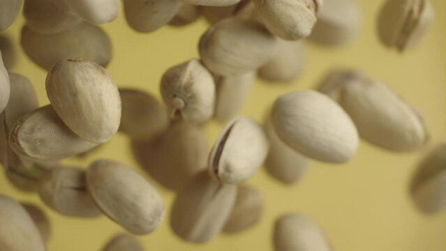 Flying in air fresh raw whole and cracked pistachios on yellow background. Pistachio nuts are falling in slow motion. Concept organic diet