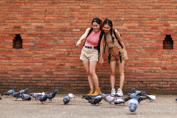 two asian tourist girl standing looking pigeons at the tha phae gate, chiang mai thailand,