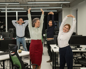 Four office workers warm up during a break. Employees do fitness exercises at the workplace. 