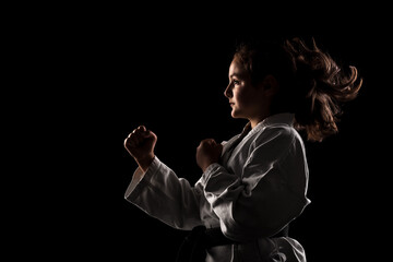 Young girl exercising karate. Child in kimono against black background. - obrazy, fototapety, plakaty
