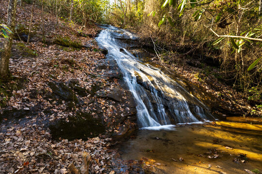 A thin waterfall cascades down a stone slope with autumn leaves surrounding it