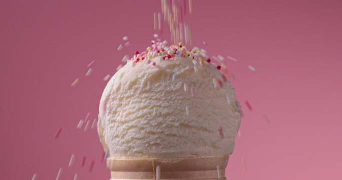 close-up of decorative sugar sprinkles falling on an ice cream ball on a pink background, slow motion video
