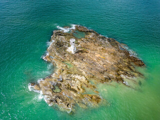 Aerial view of a small lighthouse located on a rock offshore from a tropical beach