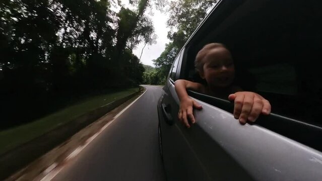 Toddler girl travels in the car and watches the road from open window enjoying the wind flow