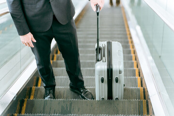 スーツケースを持ってエスカレーターを登る男性
