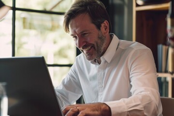 Fototapeta premium Smiling mature adult business man executive sitting at desk using laptop. Happy busy professional mid aged businessman ceo manager working on computer corporate technology in office