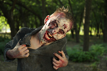 Scary zombie with bloody face outdoors. Halloween monster