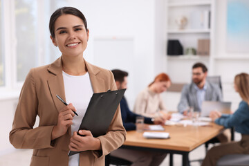 Team of employees working together in office. Happy woman with clipboard indoors