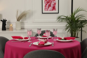 Color accent table setting. Glasses, plates, cutlery and pink napkins on table indoors