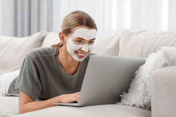 Young woman with face mask using laptop on sofa at home. Spa treatments