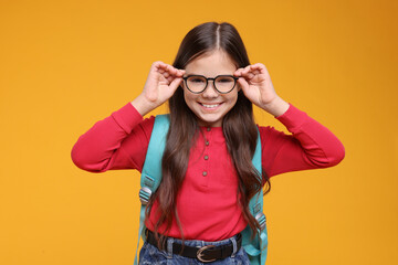 Cute schoolgirl in glasses on orange background