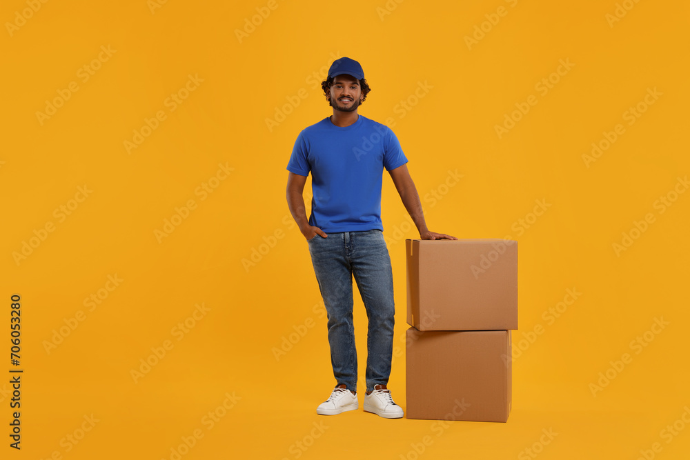 Wall mural Happy young courier with parcels on orange background