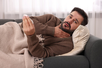 Sick man with tissue lying on sofa at home. Cold symptoms