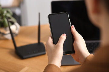 Woman with smartphone connecting to internet via Wi-Fi router at table indoors, closeup