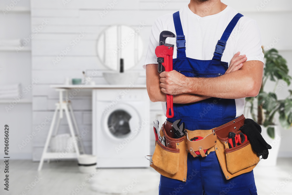 Poster plumber with pipe wrench and tool belt in bathroom, closeup. space for text