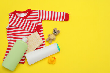Bottles of laundry detergents, baby clothes and toy bear on yellow background, flat lay. Space for...
