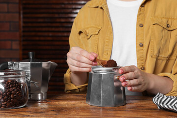 Woman putting ground coffee into moka pot at wooden table, closeup