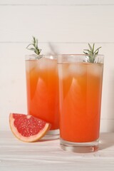 Tasty grapefruit drink with ice and rosemary in glasses on white wooden table