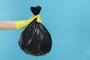 Woman holding plastic bag full of garbage on light blue background, closeup. Space for text