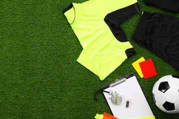 Fototapeta premium Uniform, soccer ball and other referee equipment on green grass, flat lay. Space for text