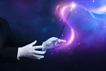 Magician with wand showing trick on dark blue background, closeup © New Africa