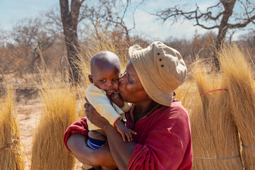 portrait of an village african woman holding her grandchild, outdoors crop of thatch in the bush