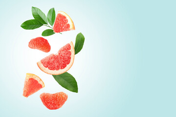 Fresh grapefruit pieces and green leaves falling on light blue background. Space for text