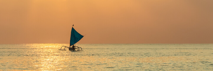 Silhouette of outrigger sailboat at sunset in Bali, Indonesia.