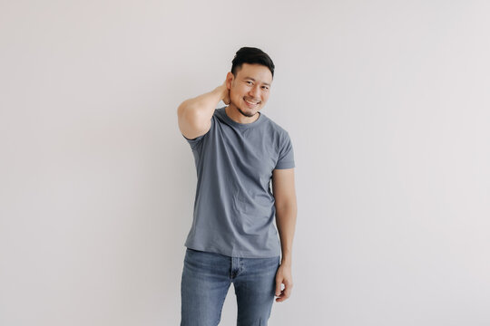 Shy and embarrassment funny asian man in blue t-shirt isolated on white wall.