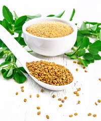 Fenugreek in spoon and bowl with leaves on light wooden board