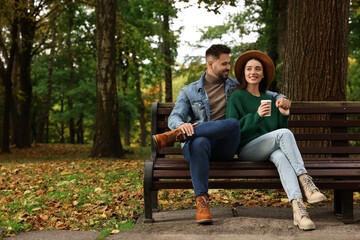 Happy young couple spending time together on wooden bench in autumn park, space for text