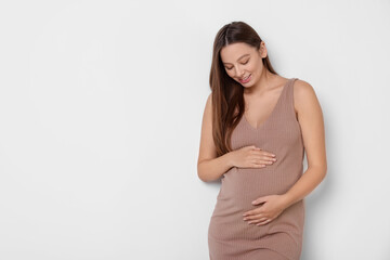 Obraz premium Beautiful pregnant woman in beige dress on white background, space for text