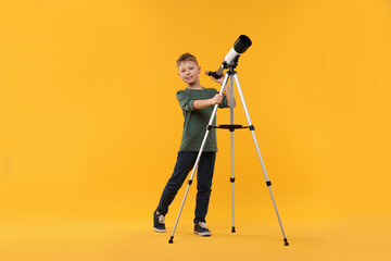 Happy little boy with telescope on orange background