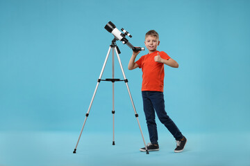 Happy little boy with telescope showing thumb up on light blue background