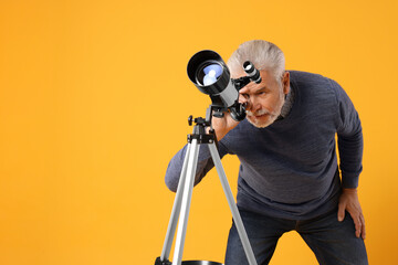 Senior astronomer looking at stars through telescope on yellow background, space for text