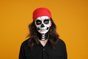 Man in scary pirate costume with skull makeup on orange background. Halloween celebration