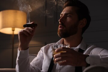 Handsome man with glass of whiskey smoking cigar at home