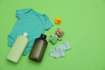 Bottles of laundry detergents, baby clothes and toys on light green background, flat lay. Space for...